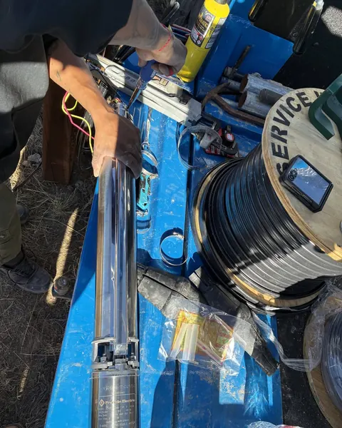 Hands wiring a stainless submersible pump motor laid out on the truck deck next to a spool of pump wire.